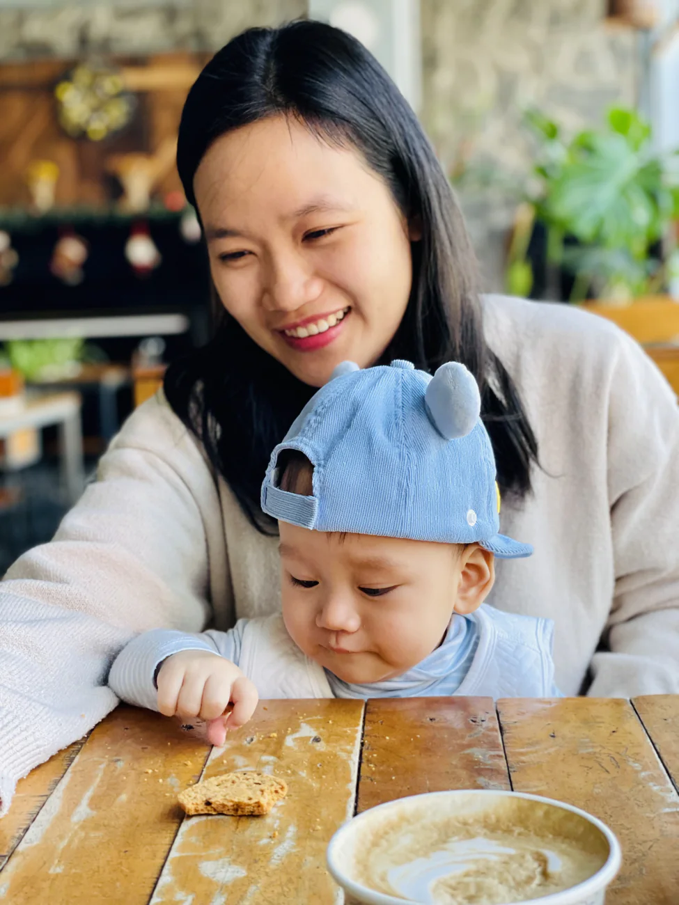 Ly smiling at a café table with a baby in a blue cap on her lap