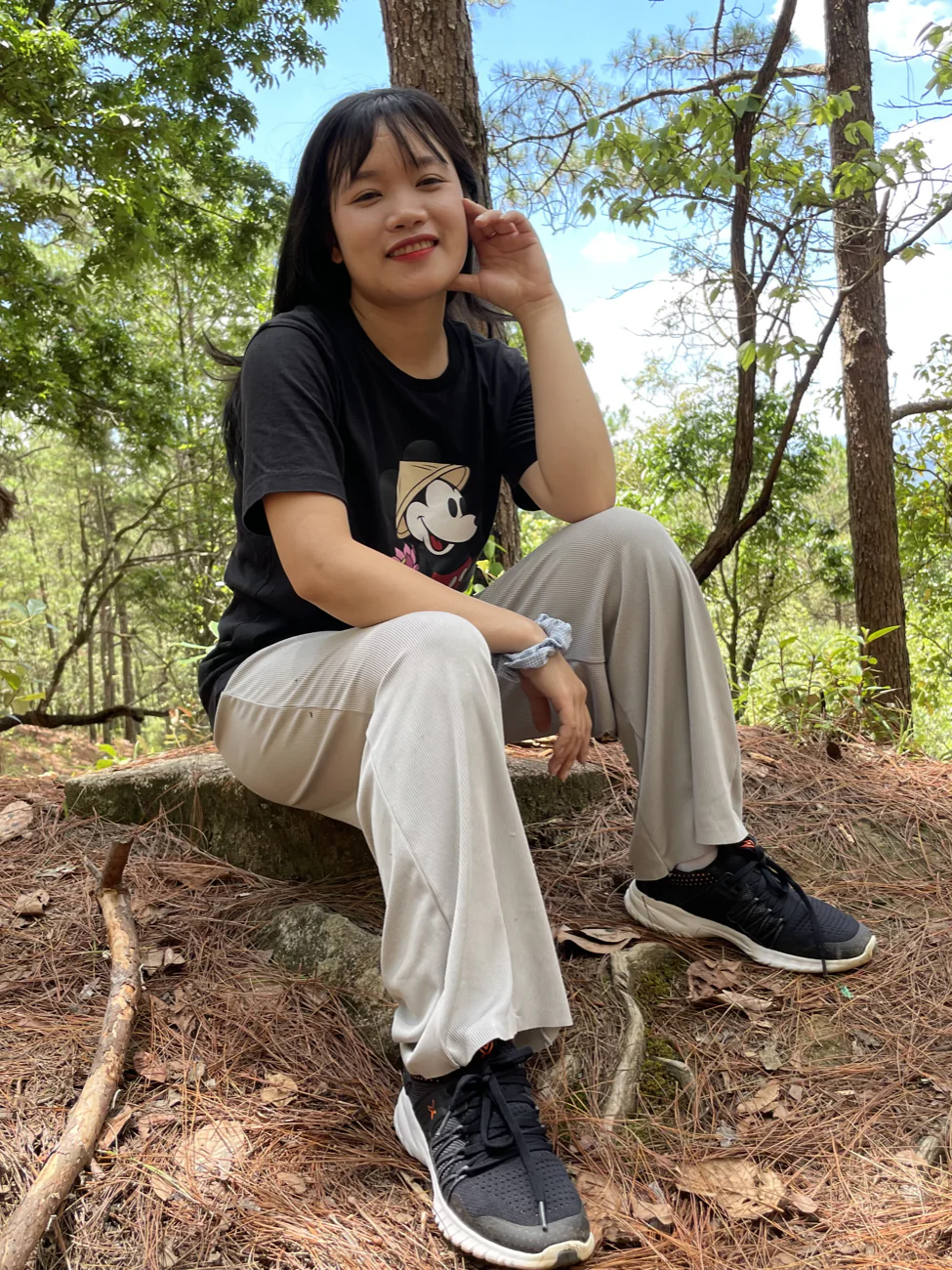 Ly sitting on a mossy rock in the forest, smiling