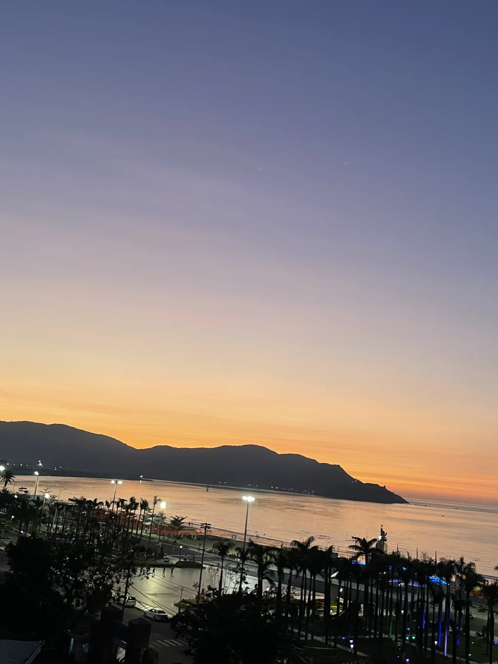 Sunset glowing orange over Quy Nhon bay and the palm-lined square