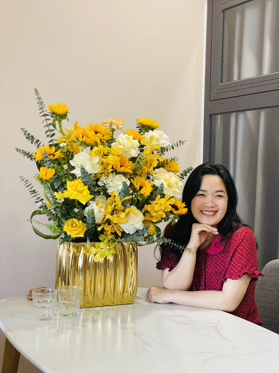 Ly beside a golden vase overflowing with sunflowers and roses